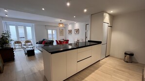 Une cuisine moderne dotée d’un îlot central, de meubles blancs et d’un coin repas avec des chaises rouges.