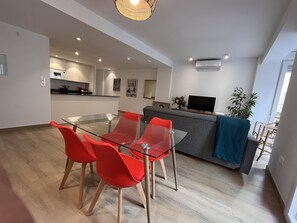 Un soggiorno moderno con un tavolo da pranzo in vetro, sedie rosse, un divano grigio e una televisione su un mobile in legno.