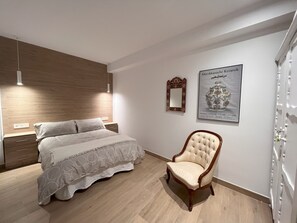 Una camera da letto con testiera in legno, un letto con copripiumino decorato, una sedia, uno specchio e un quadro appeso al muro.