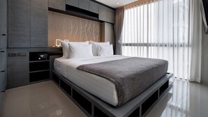 Une chambre à coucher moderne, dotée d’un grand lit, de rangements intégrés et d’une grande fenêtre agrémentée de rideaux légers.