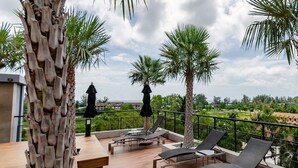 Une terrasse en bois, dotée de chaises longues et de parasols, qui offre une vue imprenable sur un paysage magnifique, avec des palmiers et la mer à l’horizon.