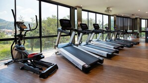 Une salle de sport équipée de tapis de course et d’un appareil elliptique, dotée de grandes fenêtres et offrant une vue sur la verdure.