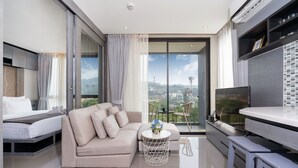 Un salon moderne avec un canapé, une petite table ronde, un téléviseur et un balcon offrant une vue sur la ville.