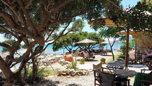An outdoor seating area with tables and chairs, a stone wall, and a view of the sea.