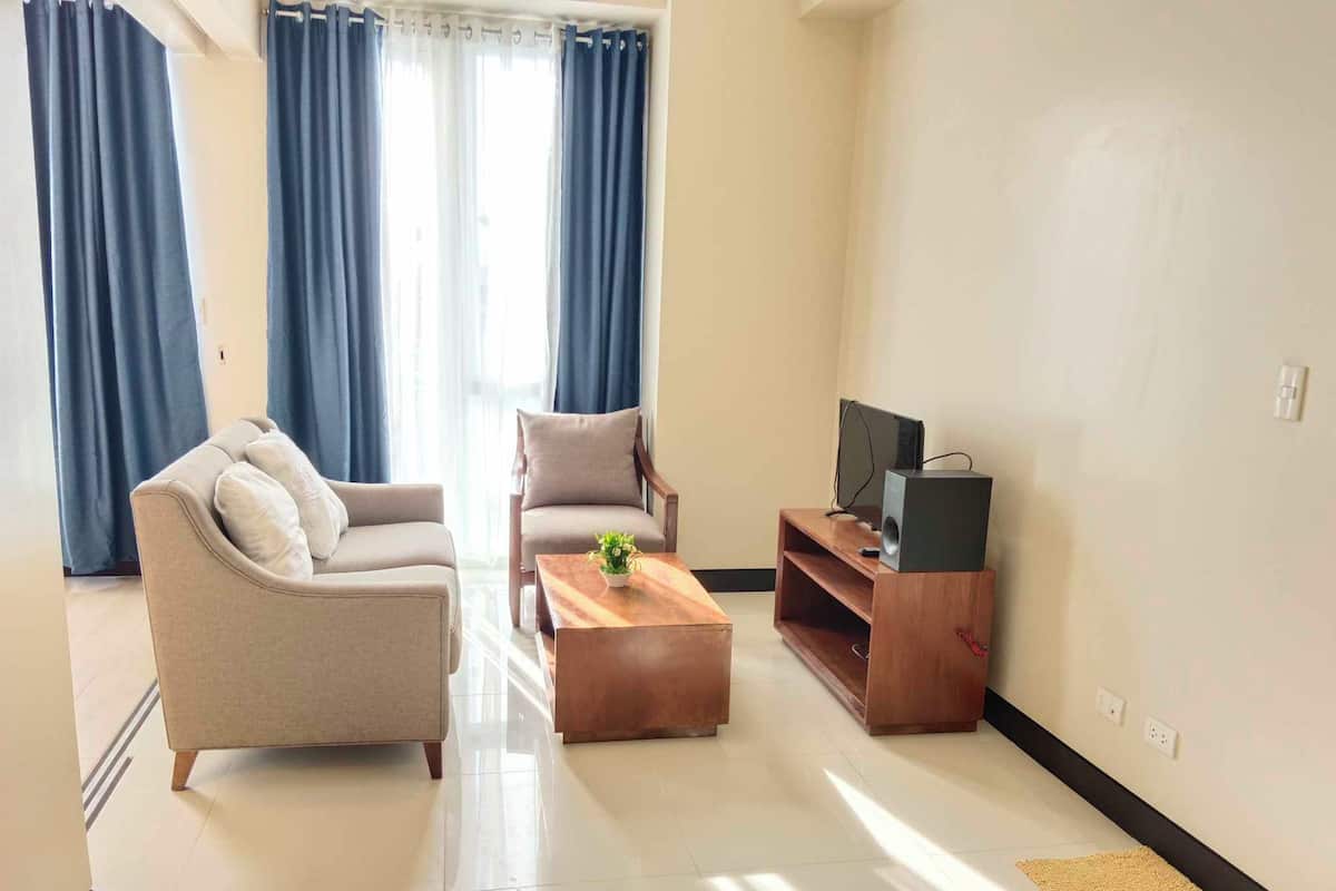 Een woonkamer met een bank, fauteuil, salontafel, tv-meubel en gordijnen.