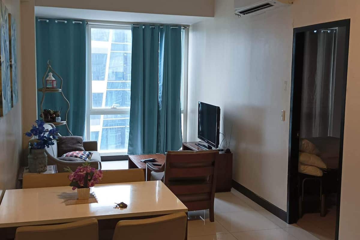 Een woonkamer met een eettafel, stoelen, een televisie en een raam met gordijnen.