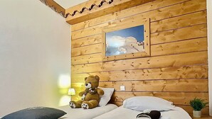 A wooden cabin-style room with two beds, a teddy bear, a lamp, and a small plant.