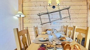 A wooden dining table with chairs, a lamp, and a tray of pastries and bread.