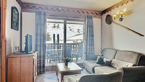 A living room with a sofa, a wooden cabinet, a television, and a view of the outdoors through a glass door.