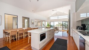 Une cuisine spacieuse dotée d’un grand îlot central, d’une table à manger en bois et de chaises. Une porte-fenêtre coulissante donne accès à un balcon aménagé avec des meubles d’extérieur.
