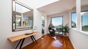 Un intérieur moderne avec une console en bois, un fauteuil suspendu et de grandes fenêtres donnant sur l’extérieur.