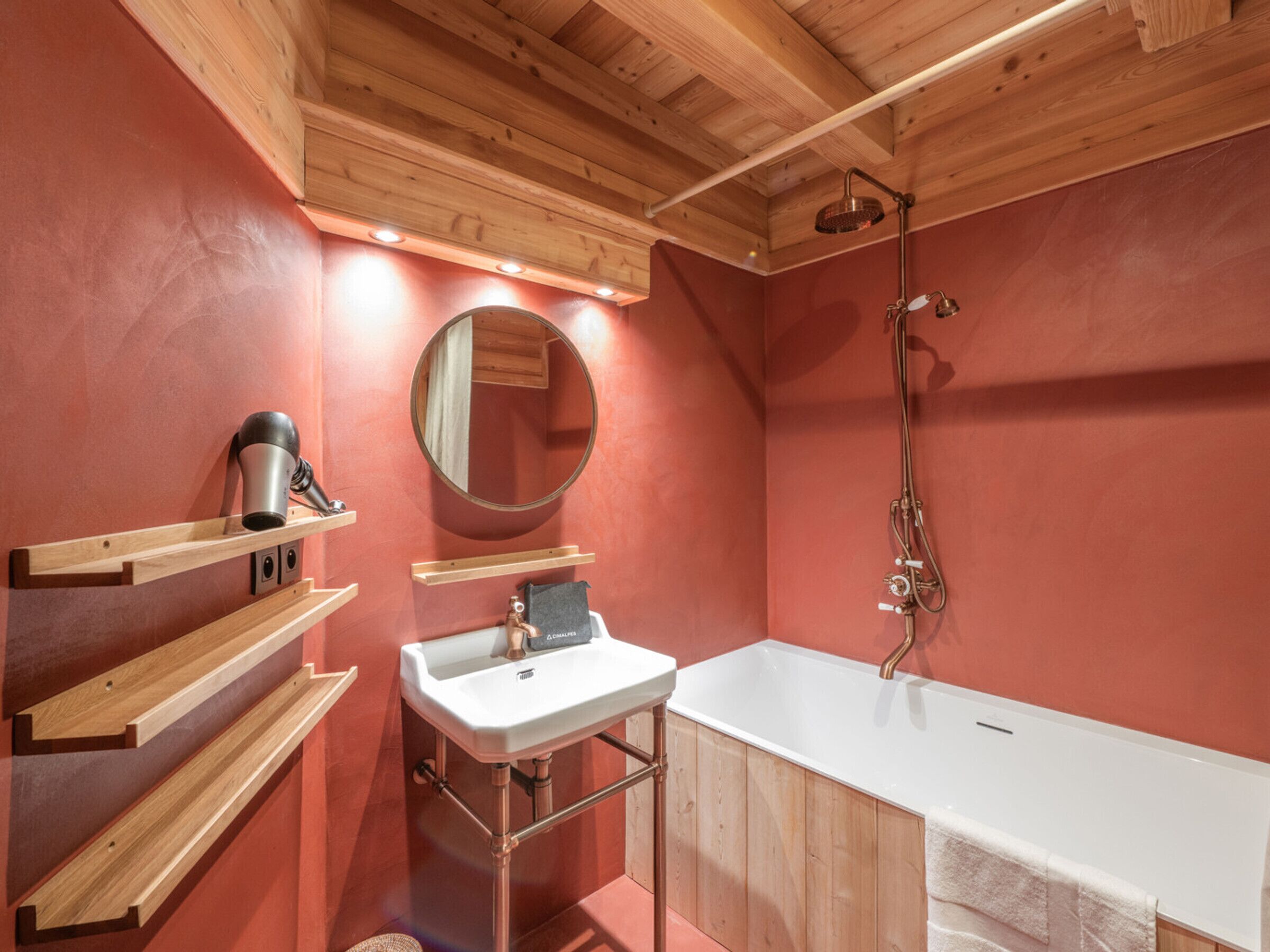 A bathroom with a wooden ceiling, a white sink, a bathtub, and wooden shelves.