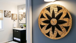 Une salle de bain moderne avec un meuble-lavabo noir, une décoration murale ronde en fibres tressées et des motifs de feuilles encadrées sur le mur.