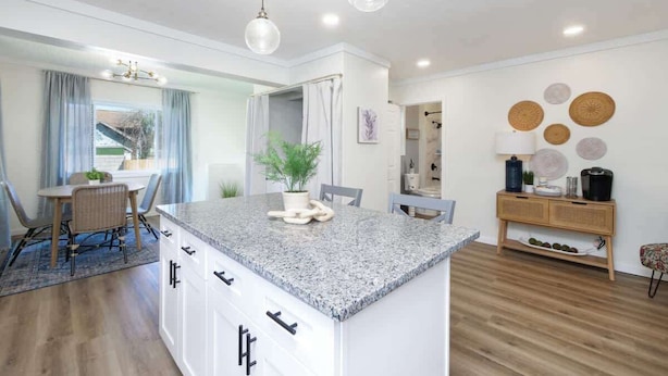Une cuisine moderne dotée d’un îlot en granit, de meubles blancs et d’un coin repas avec une table et des chaises.
