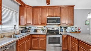 A kitchen with wooden cabinets, a microwave, a stove, and a dishwasher. - Single Story Henderson 3BR Home, Hot tub, Sleeps 6 (Henderson)