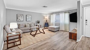 A living room with a sofa, coffee table, and armchair, a flat-screen TV, and a lamp. - Single Story Henderson 3BR Home, Hot tub, Sleeps 6 (Henderson)