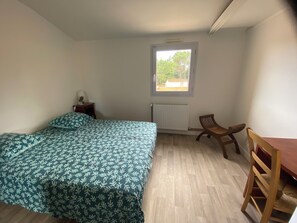 A bedroom with a bed, a chair, a small table, a radiator, and a window.