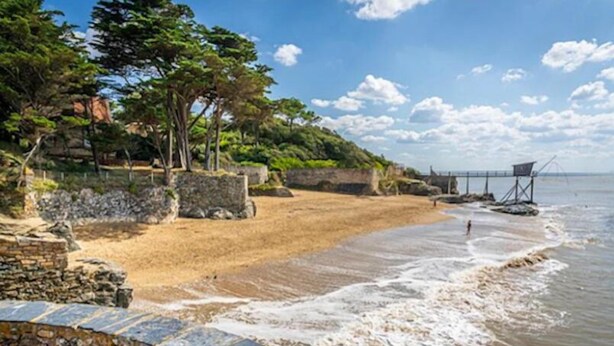 Una playa con un muro de piedra, un paseo de madera y un puente al fondo.
