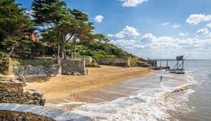 A beach with a stone wall, a wooden walkway, and a bridge in the background. - La Baie: Family Home for 10 People on the Jade Coast (shared garden) (La Bernerie-en-Retz)