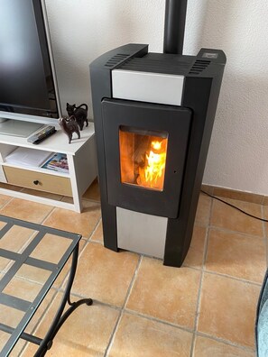 A modern wood-burning stove with a glass door, a television, and a small figurine on a white cabinet.