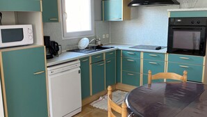 Una cocina compacta con gabinetes verde azulado, un lavavajillas blanco, una estufa negra y una mesa de comedor con sillas.