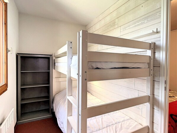 A bunk bed with a metal ladder and a shelf unit beside it.
