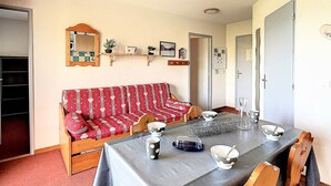 A cozy living room with a sofa, a dining table with chairs, a mirror, and wall-mounted shelves with decorative items. - PMR Apartment in Corbier, Valley View, Balcony (Le Corbier)