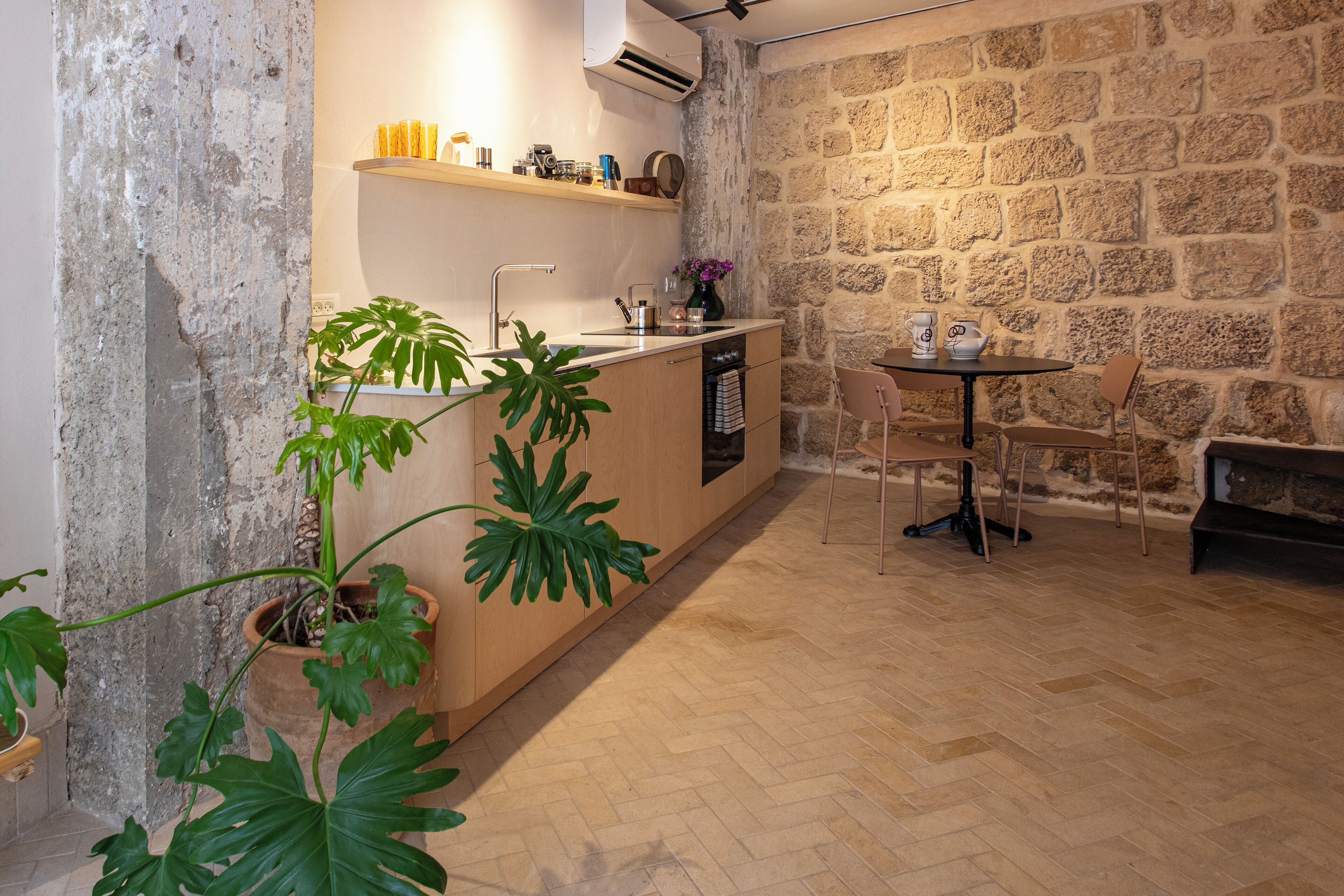A compact kitchen with a stone wall, wooden cabinets, and a small dining area with a table and chairs.