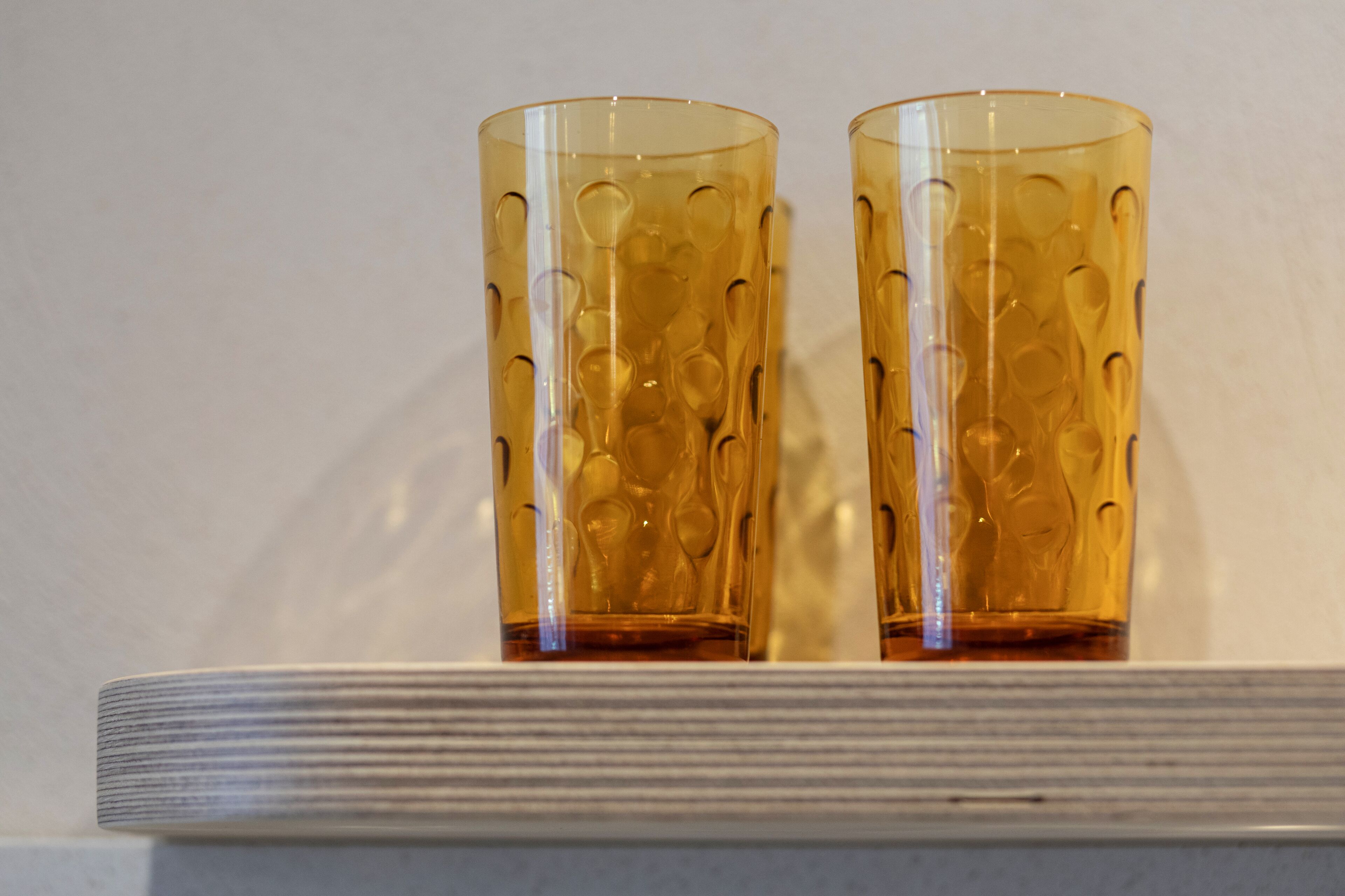 Deux verres transparents ornés d’un motif texturé, posés sur une étagère blanche devant un fond uni.