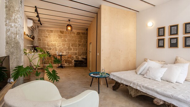 A cozy room with a white sofa, a small round table, and a chair. There is a stone wall and a wooden door in the background. - Vintage Eclectic Loft by Sea N' Rent (Tel Aviv)
