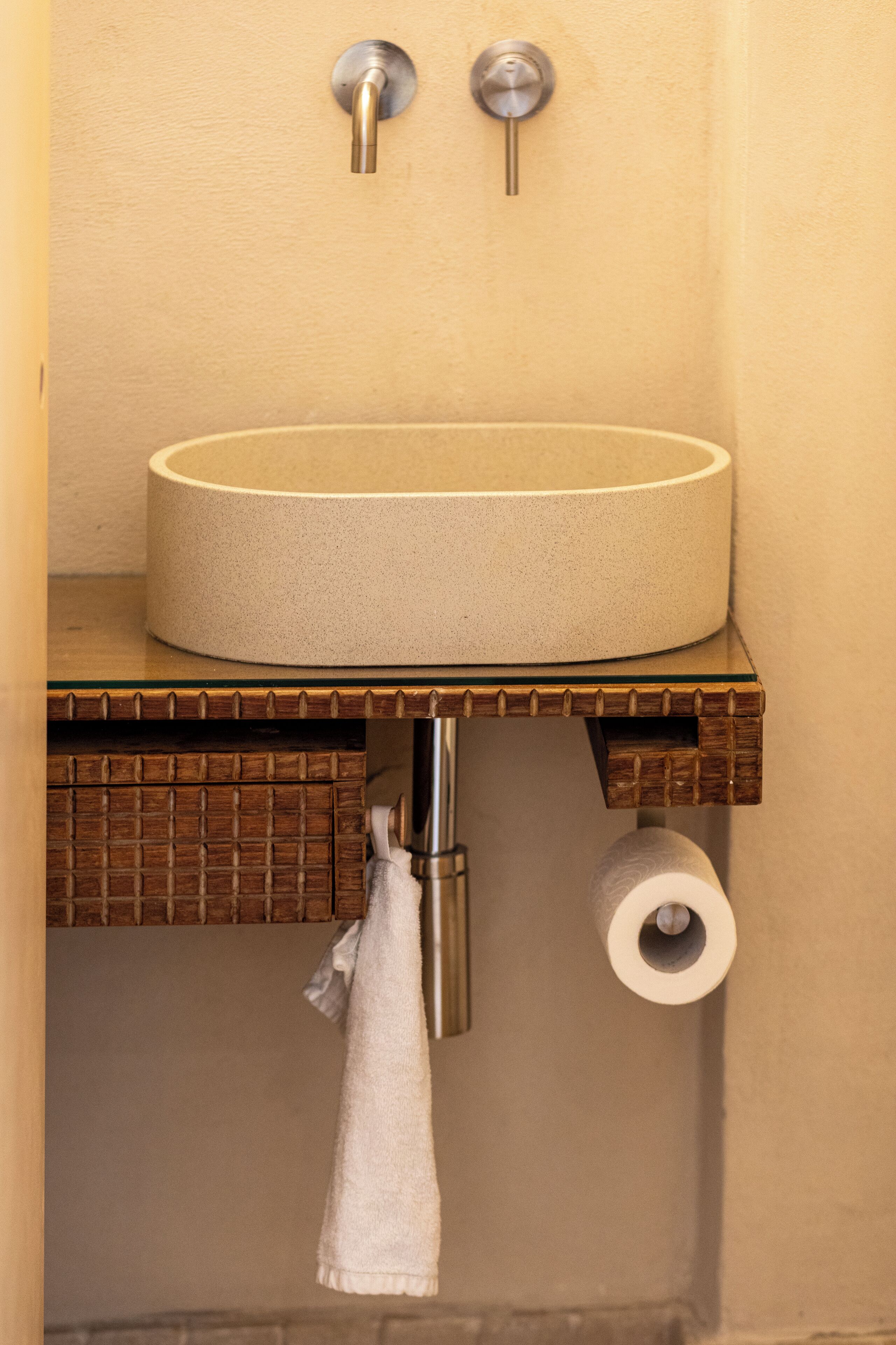 Een badkamer met een rond wastafel, een handdoek aan een rek en een toiletrol.