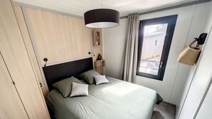 Ein Schlafzimmer mit einem Bett, einem Kleiderschrank, einem Fenster mit Vorhängen und einer hängenden Pflanzkorb.