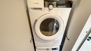 Eine THOMSON Waschmaschine mit Frontlader in einem kleinen, abgeschlossenen Waschraum mit Tür.