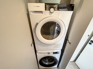 Un lave-linge THOMSON à chargement frontal, installé dans un petit espace buanderie fermé, doté d’une porte.