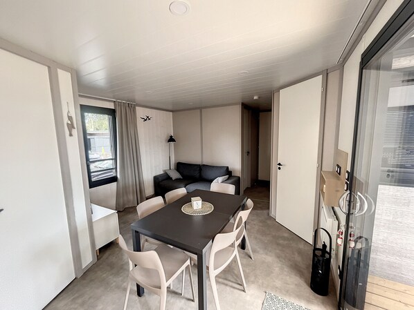 A compact living space with a dining table, chairs, a sofa, and a lamp. - Luxury Chalet in Jullouville - 6 Guests - Heated Pool - WiFi - Near Beach and Shops (Jullouville)