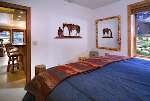 Ein Schlafzimmer mit einem großen Bett, Holzmöbeln und rustikalen Einrichtungsgegenständen, darunter eine Pferdeskulptur und ein Spiegel.