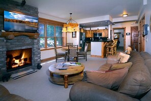 A cozy living room with a fireplace, a round coffee table, a sofa, and a television mounted on a stone wall.