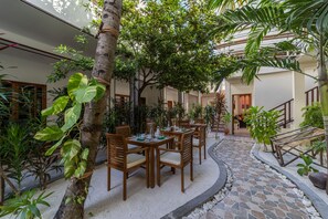 Um pátio com área de refeições, cercado por plantas e um caminho de pedra.