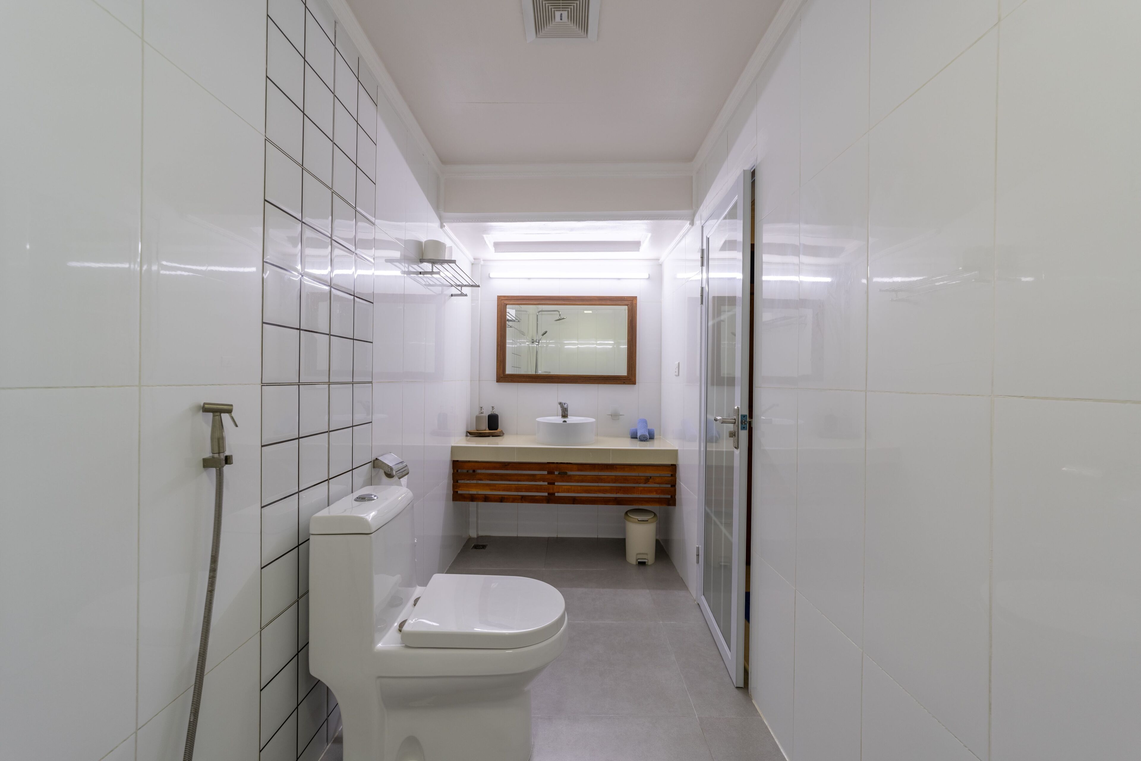 A modern bathroom with white tiles, a toilet, a sink, and a mirror.