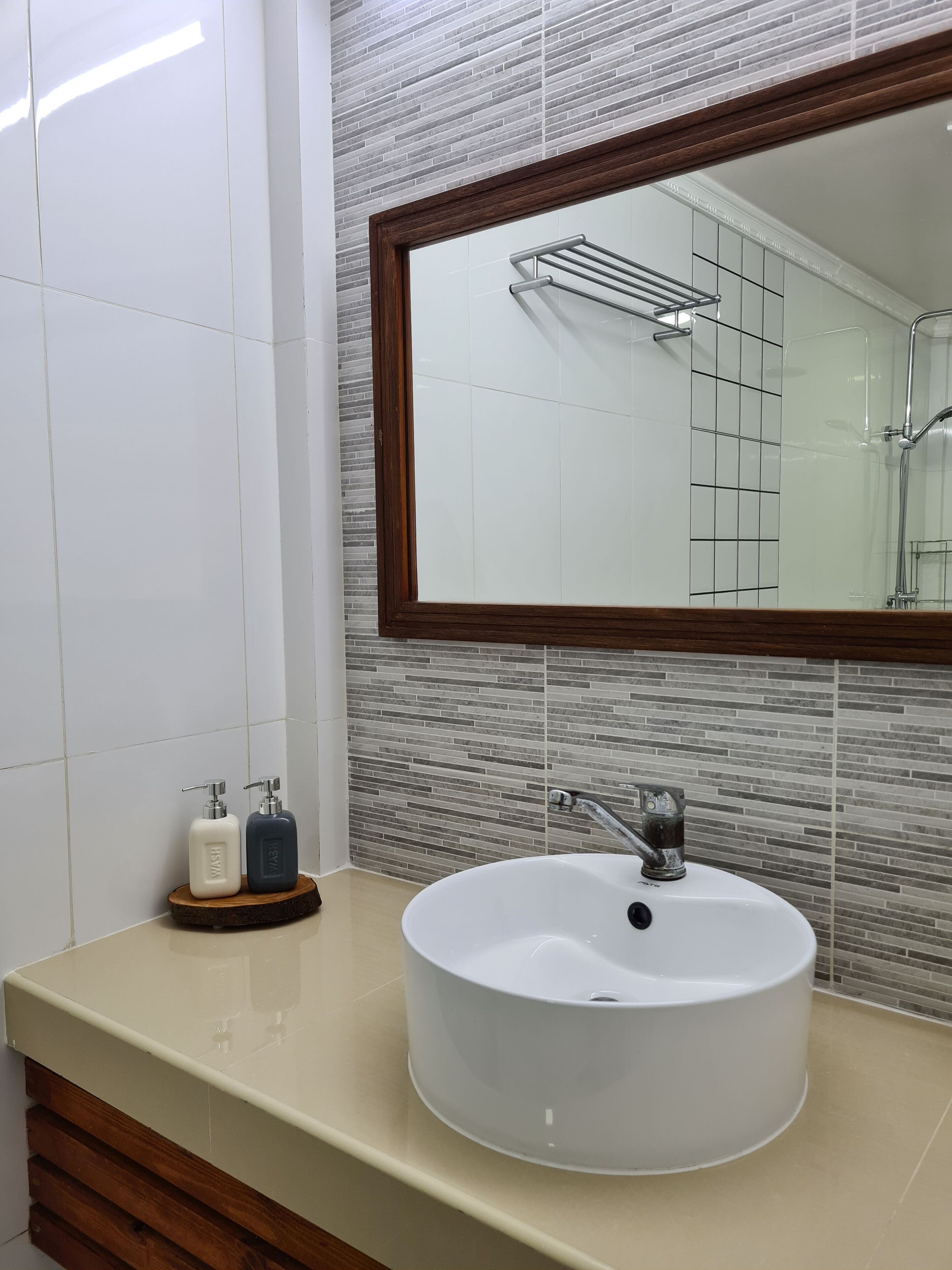 A bathroom with a white sink, a wooden vanity, a mirror with a wooden frame, and a tiled wall.