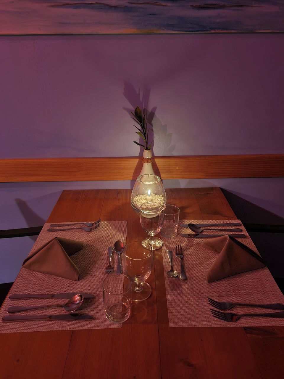 Una mesa de comedor dispuesta con un florero, una vela y un vaso de agua.