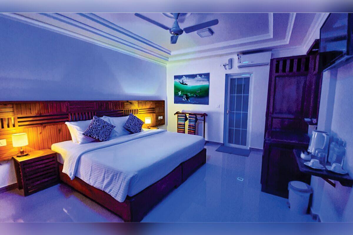 A bedroom with a large bed, bedside lamps, a ceiling fan, a door, and a small table with a coffee maker.