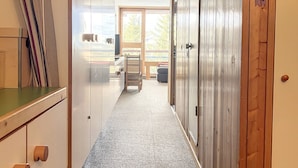 Un pasillo con una puerta de madera, una puerta de cristal que da a un balcón y una silla cerca de la puerta de cristal.