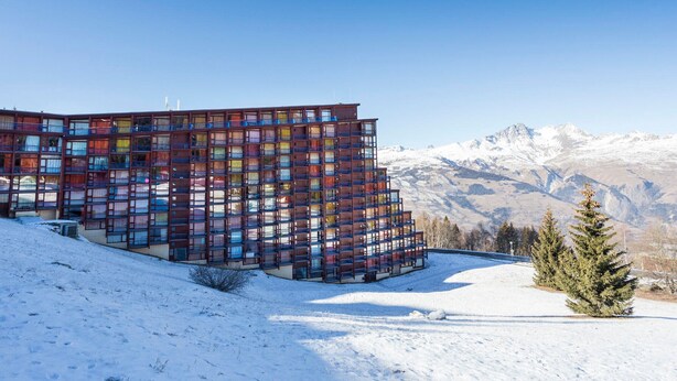 Un edificio moderno de varios pisos con una fachada singular, con vistas a una imponente montaña nevada.
