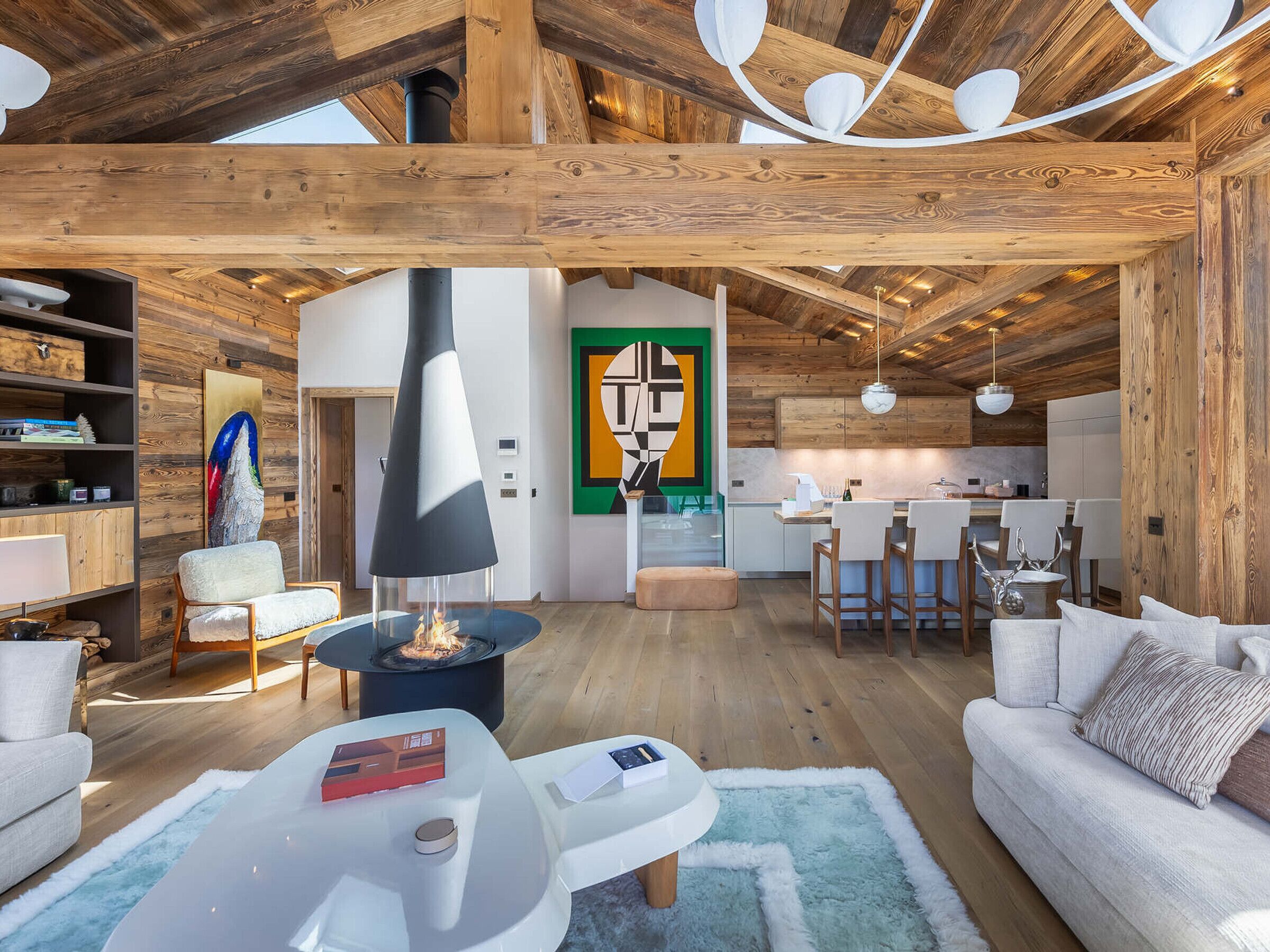 A spacious living area with a fireplace, wooden beams, and a modern kitchen in the background.