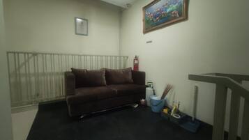 Una habitación con un sofá marrón, un cuadro de peces, un extintor y un cubo azul con productos de limpieza.