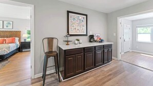 Een moderne keuken met een centraal eiland, een eethoek met een stoel, en een slaapkamer met een bed en nachtkastje.