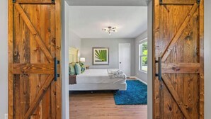 Een slaapkamer met een bed, een blauw vloerkleed, een plafondventilator en een lijst met een afbeelding aan de muur.