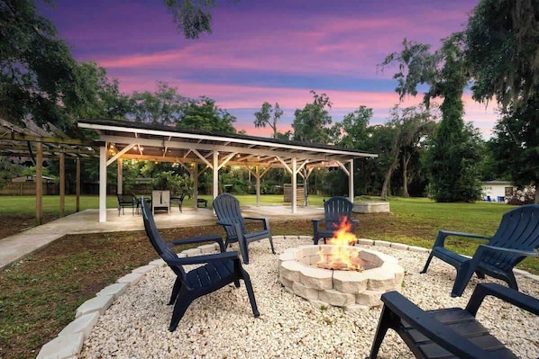 A covered outdoor seating area with Adirondack chairs, a fire pit, and a pergola.