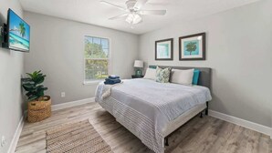 A bedroom with a bed, a ceiling fan, a window, and a wall-mounted TV. - Coconut Cove (Jacksonville Beach)